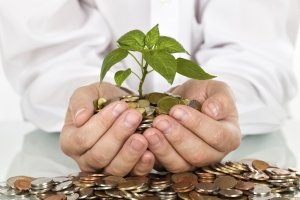 Businessman holding plant sprouting from a handful of coins - good investment and money concept